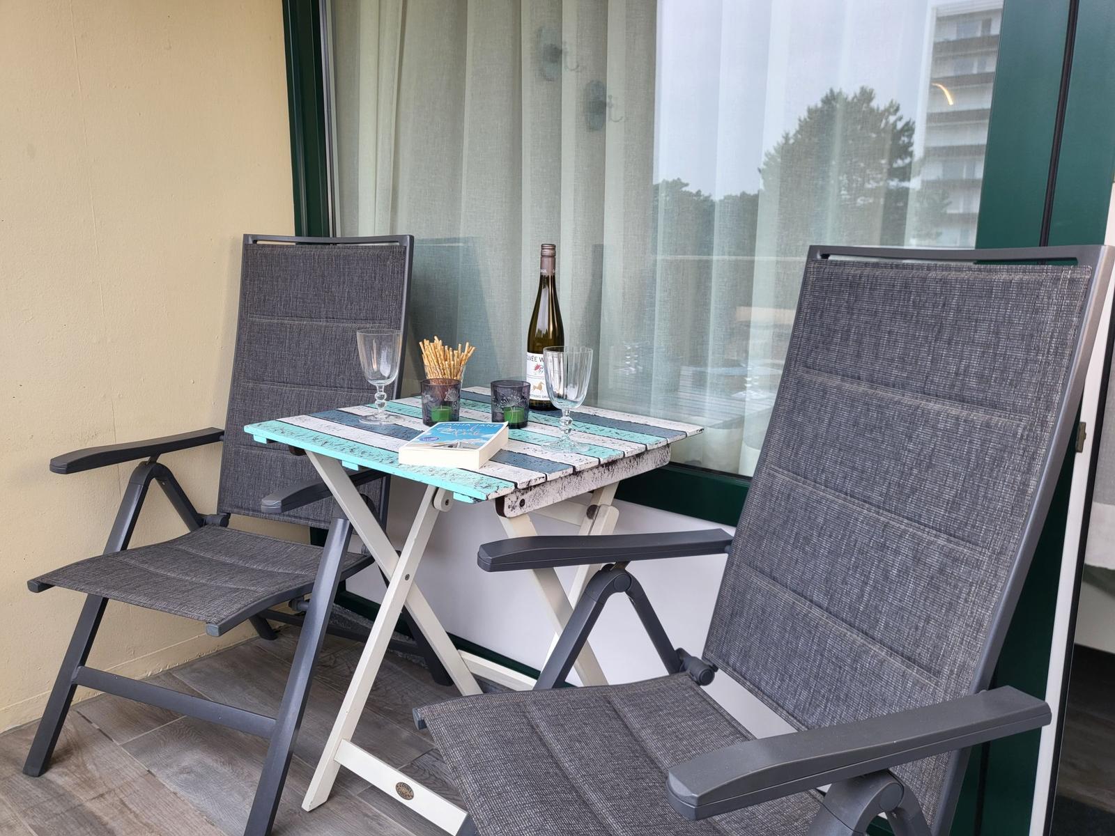 Terrasse mit zwei Stühlen, Tisch und Weinflasche. Durchsichtige Fensterfront.