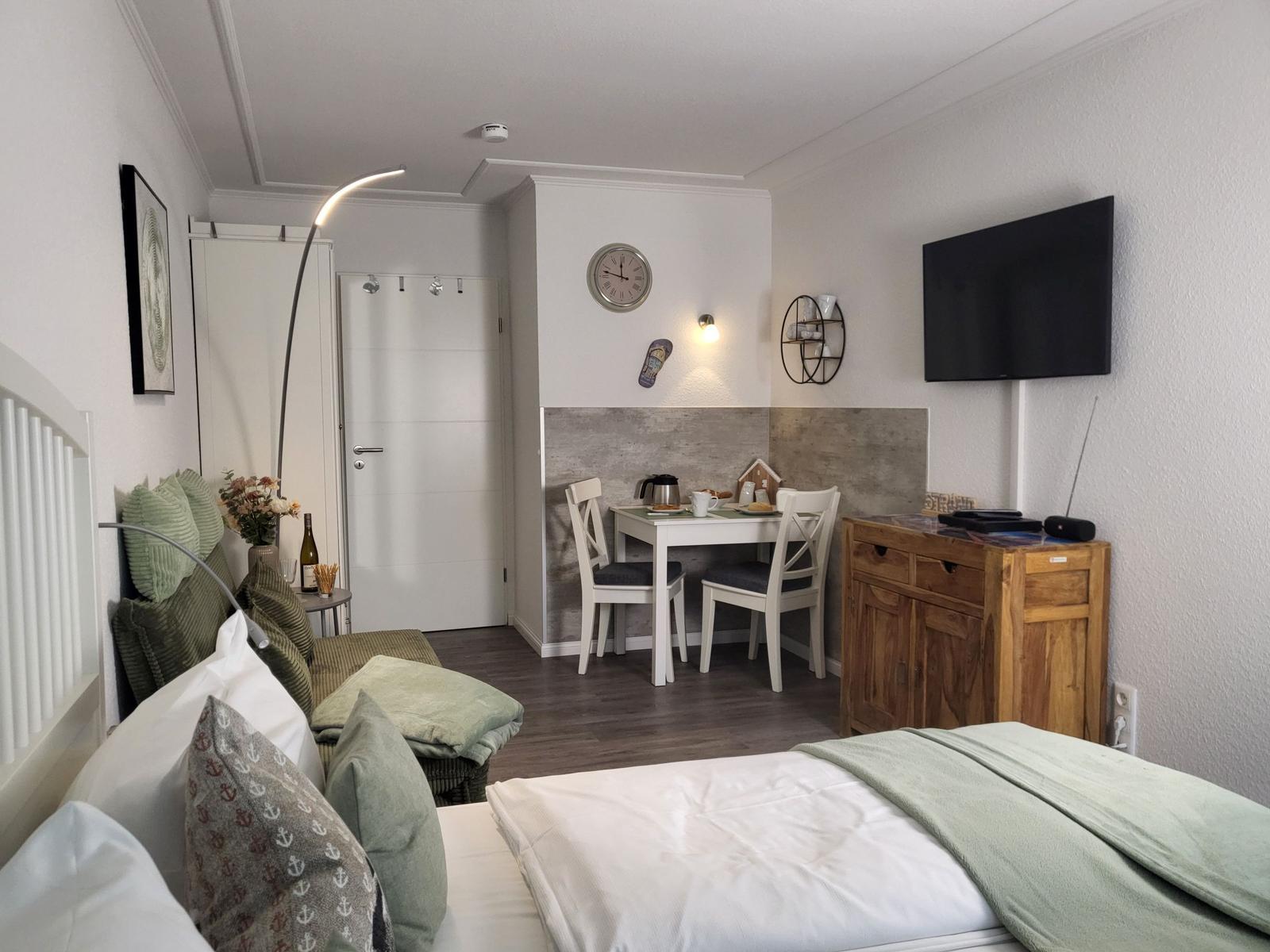 Schlafzimmer mit Bett, Sitzgelegenheit, Esstisch und Fernseher an der Wand.