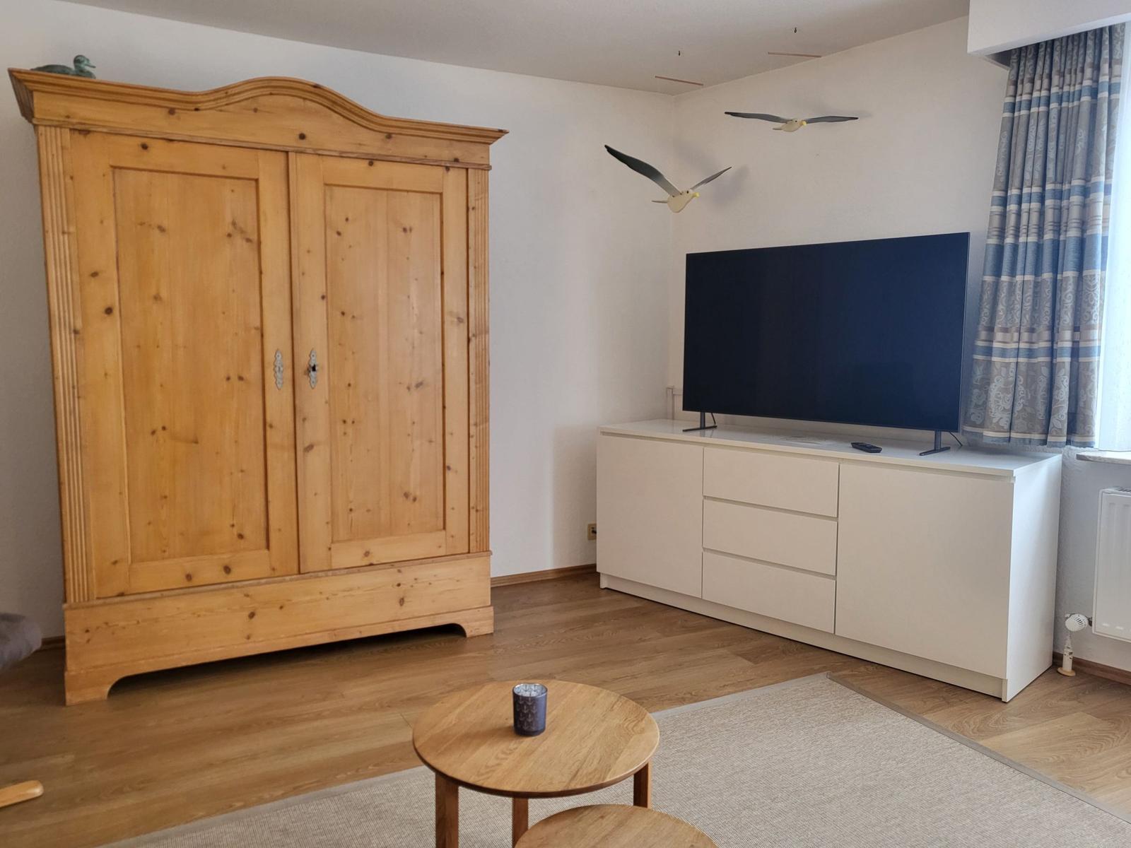 Wohnzimmer mit Holzschrank, Fernseher und runden Tisch.