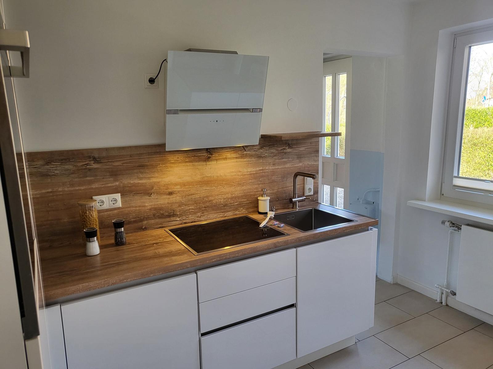 Kitchen with wooden backsplash, stainless steel sink, and modern range hood.