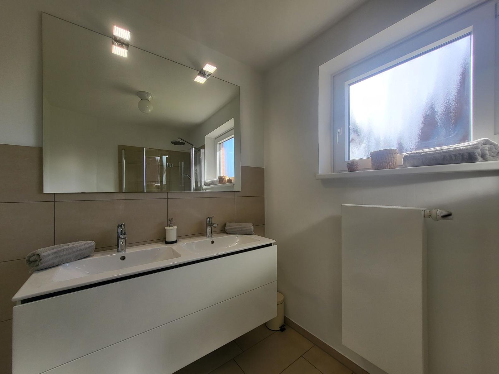 Bathroom with sink, mirror, and window. Shower visible in mirror.