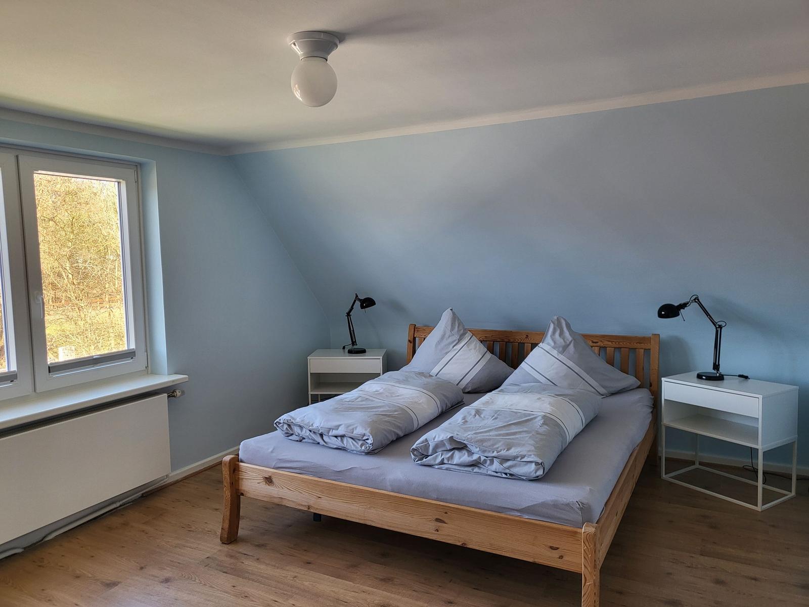 Bedroom with wooden bed, two nightstands, and window with view of trees.
