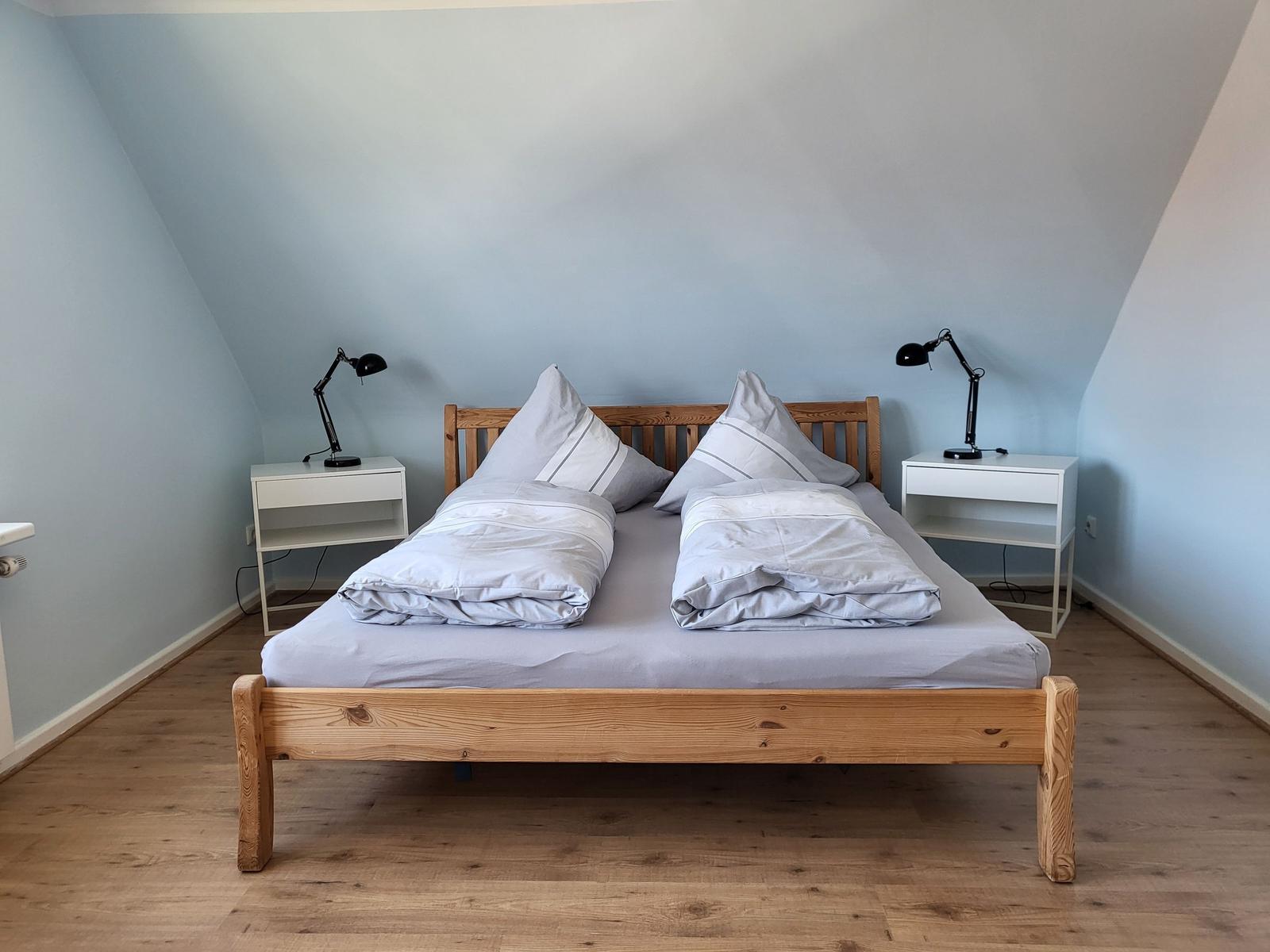 Bedroom with wooden bed, two nightstands, and lamps against sloped walls.