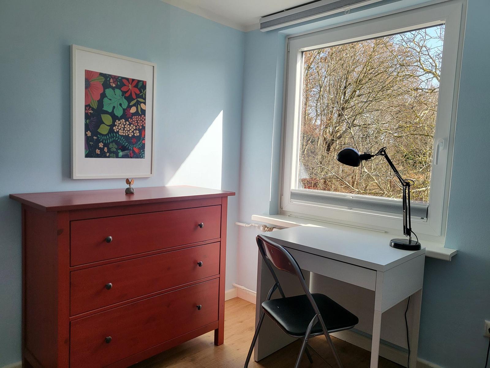 A room with blue walls, a red dresser, and a white desk with chair.