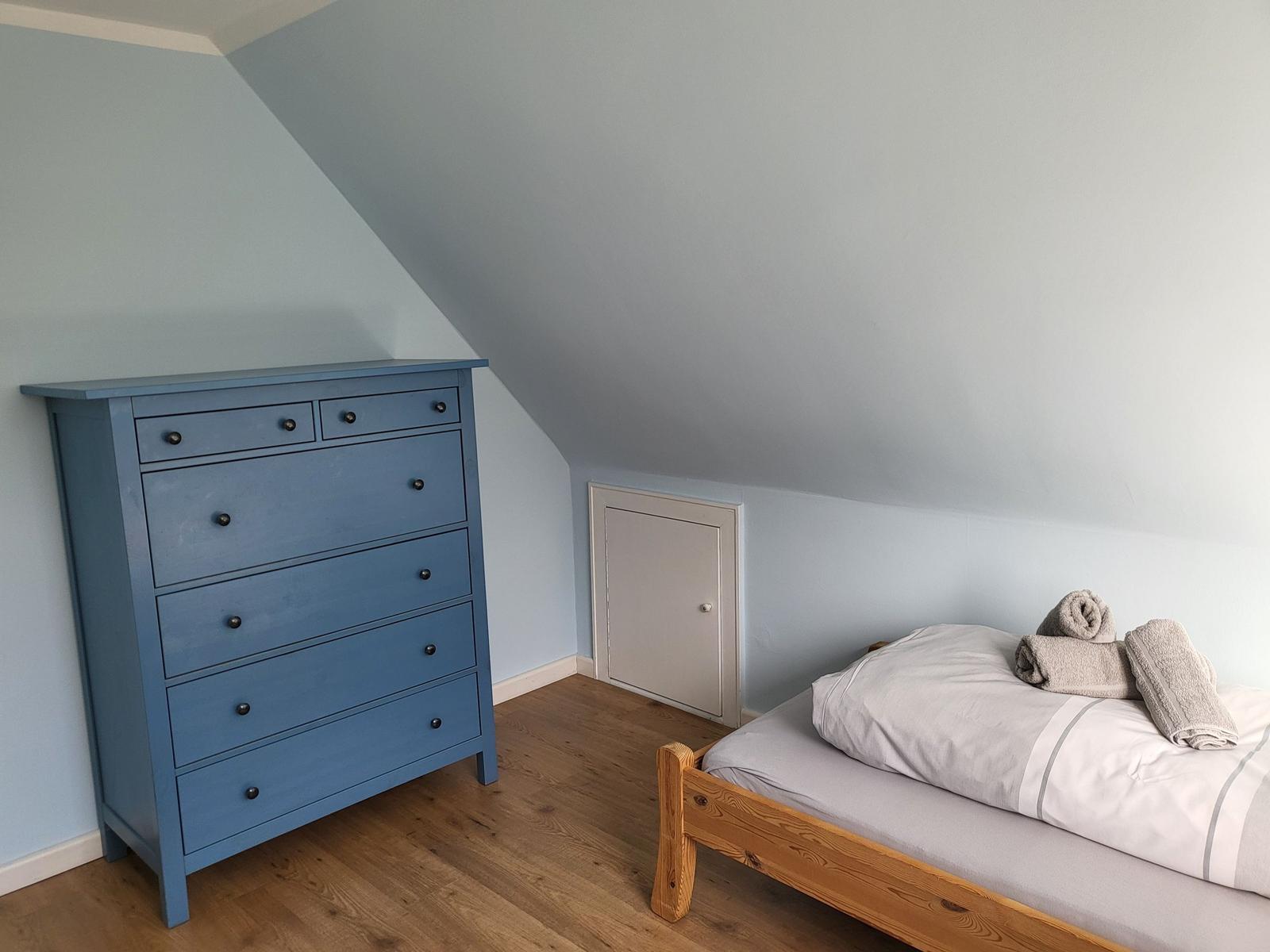 Bedroom with wooden bed, blue dresser, and sloped ceiling.