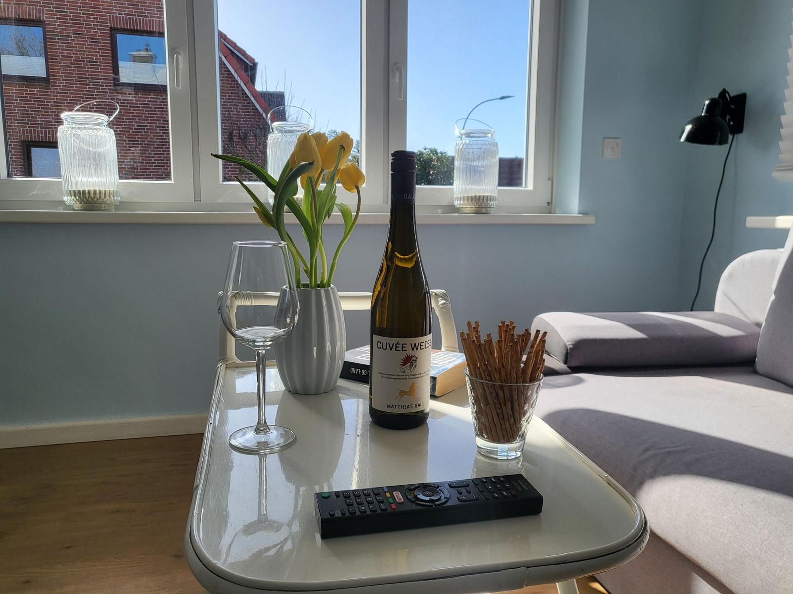 Table with wine, tulips, and snacks by window overlooking buildings.