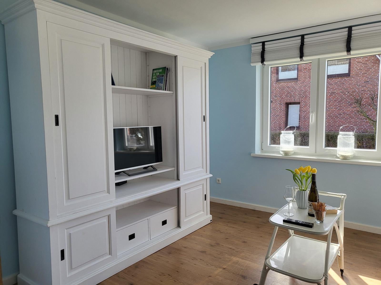 Living room with white TV cabinet, window with lantern and table with flowers.