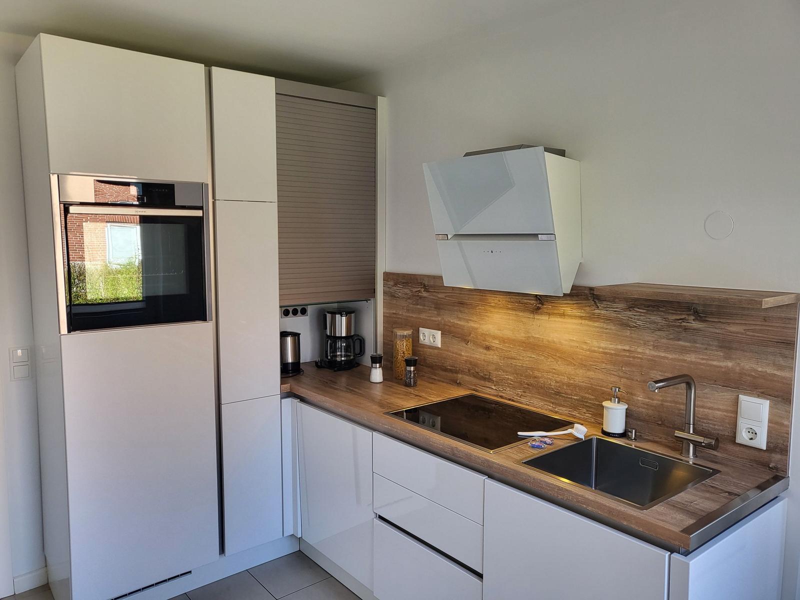 Kitchen with white cabinets, wooden backsplash, and stainless steel sink.