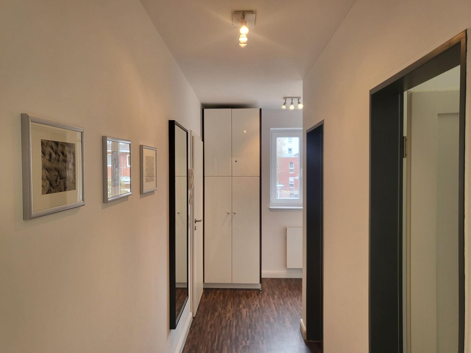 Flur mit Bildern, Schrank und Fenster. Holzboden und Türen.