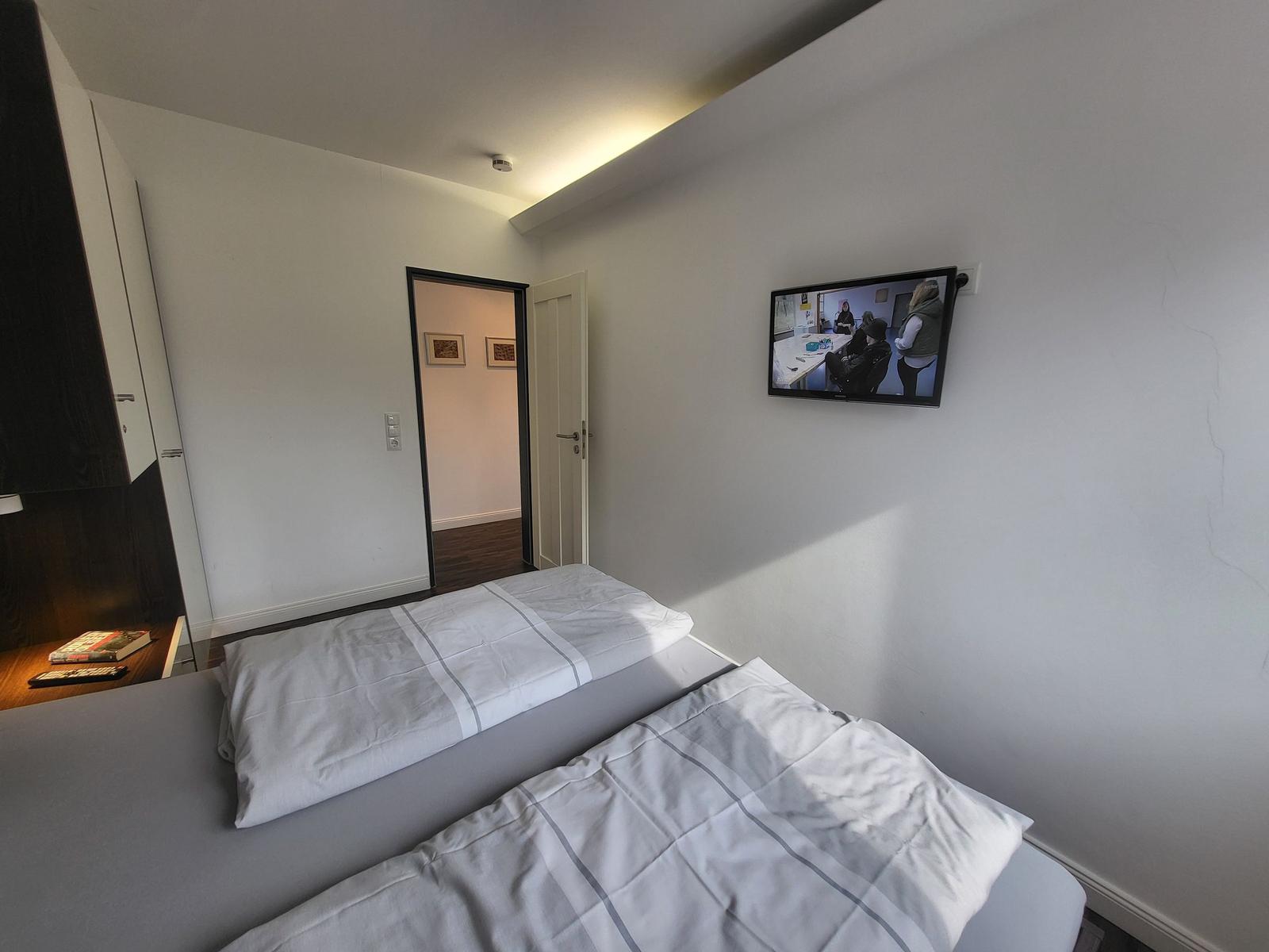 Schlafzimmer mit Doppelbett, Wand-TV und Zugang zu einem Flur.