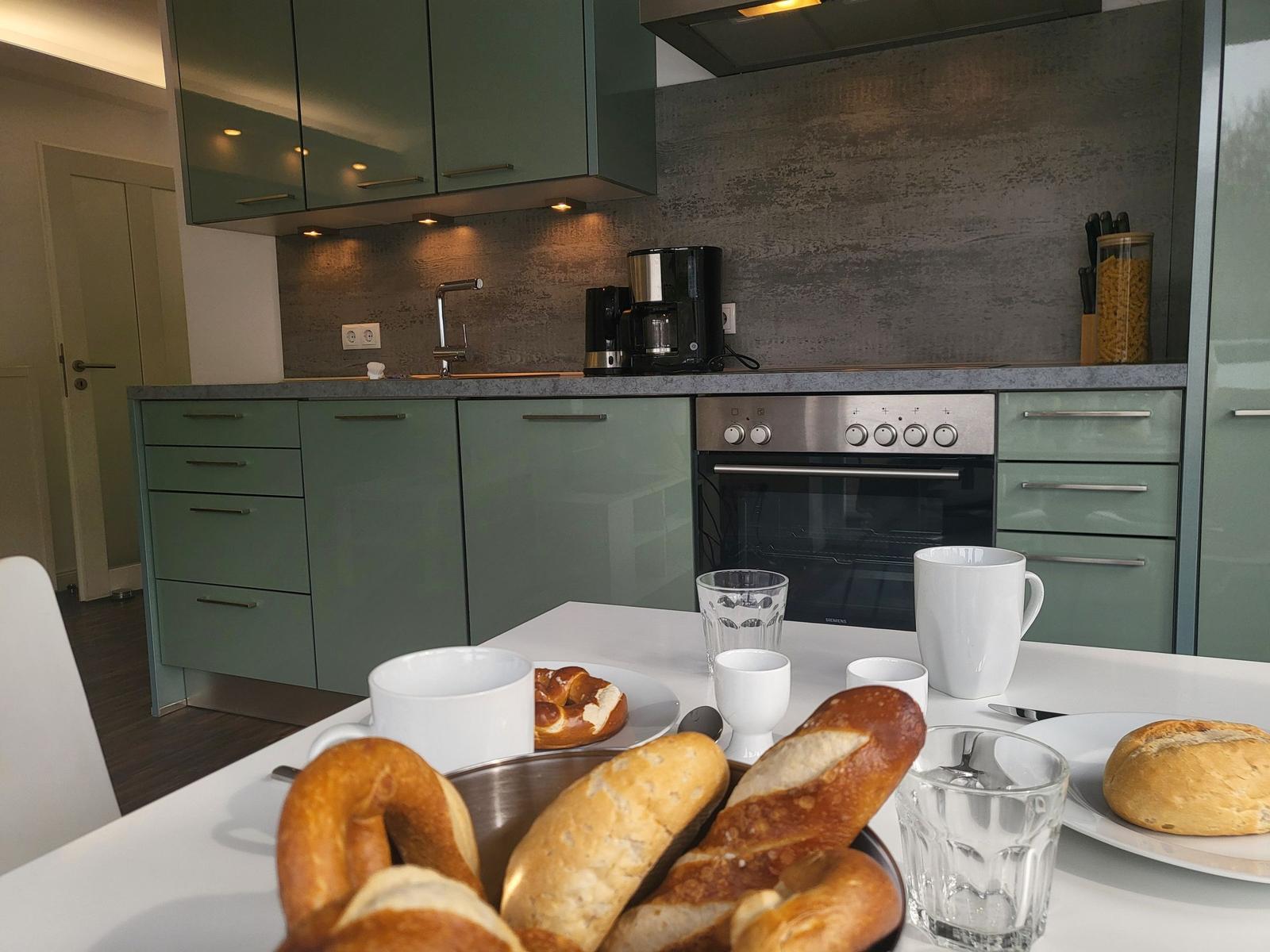 Küche mit grünen Schränken und Frühstückstablett mit Brot und Tassen.