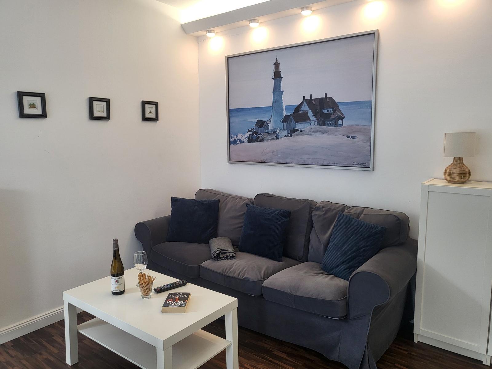 Ein Wohnzimmer mit grauem Sofa, weißem Tisch und Wandbild mit Leuchtturm.