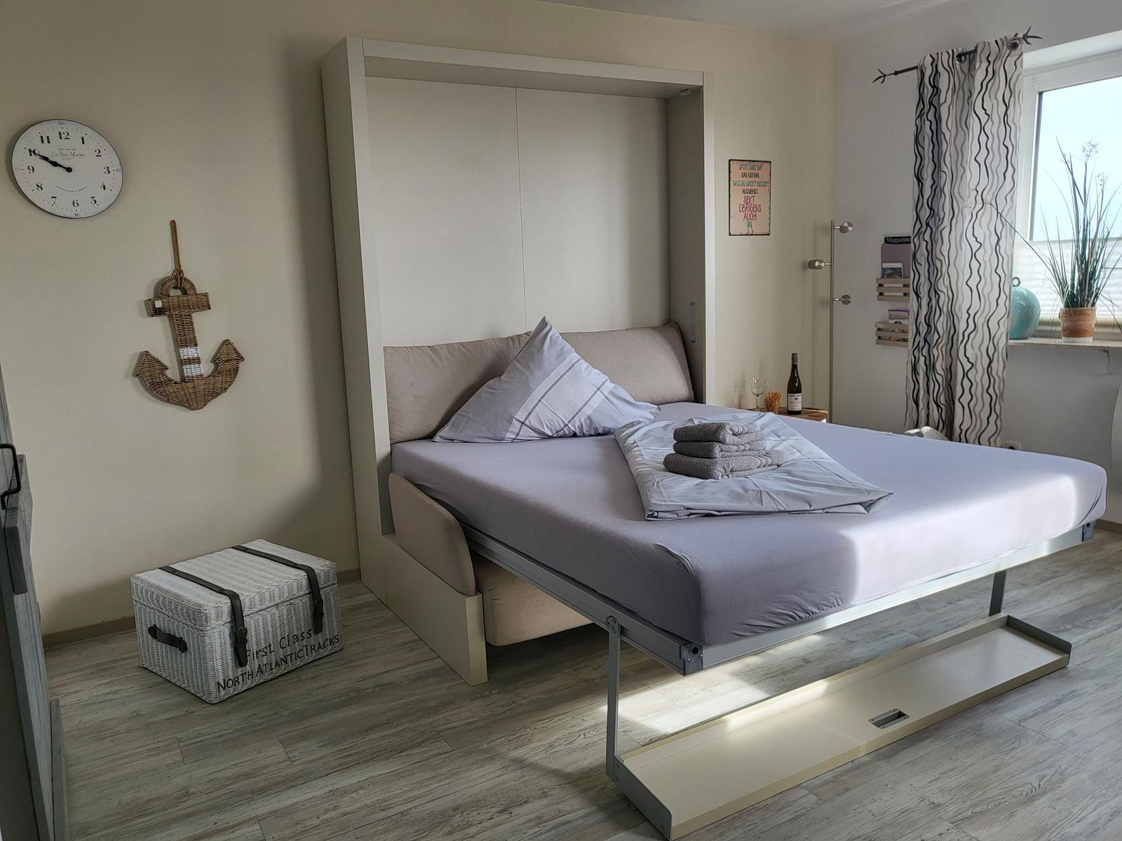 Schlafzimmer mit Aufbewahrungsbett, Wanduhr und Stehlampe.