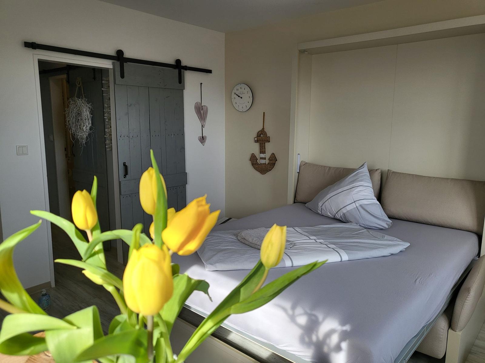 Schlafzimmer mit Bett, Tür und Tulpen im Vordergrund.