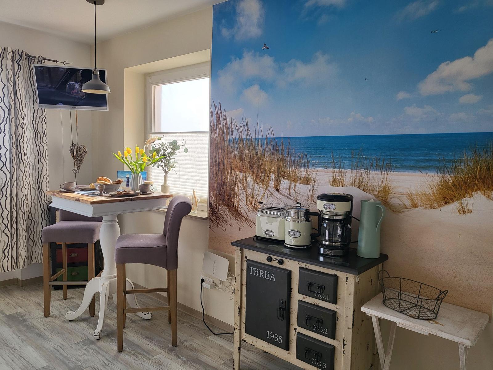 Küche mit Küchenzeile, Tisch, Stühlen und Strandbild an der Wand.