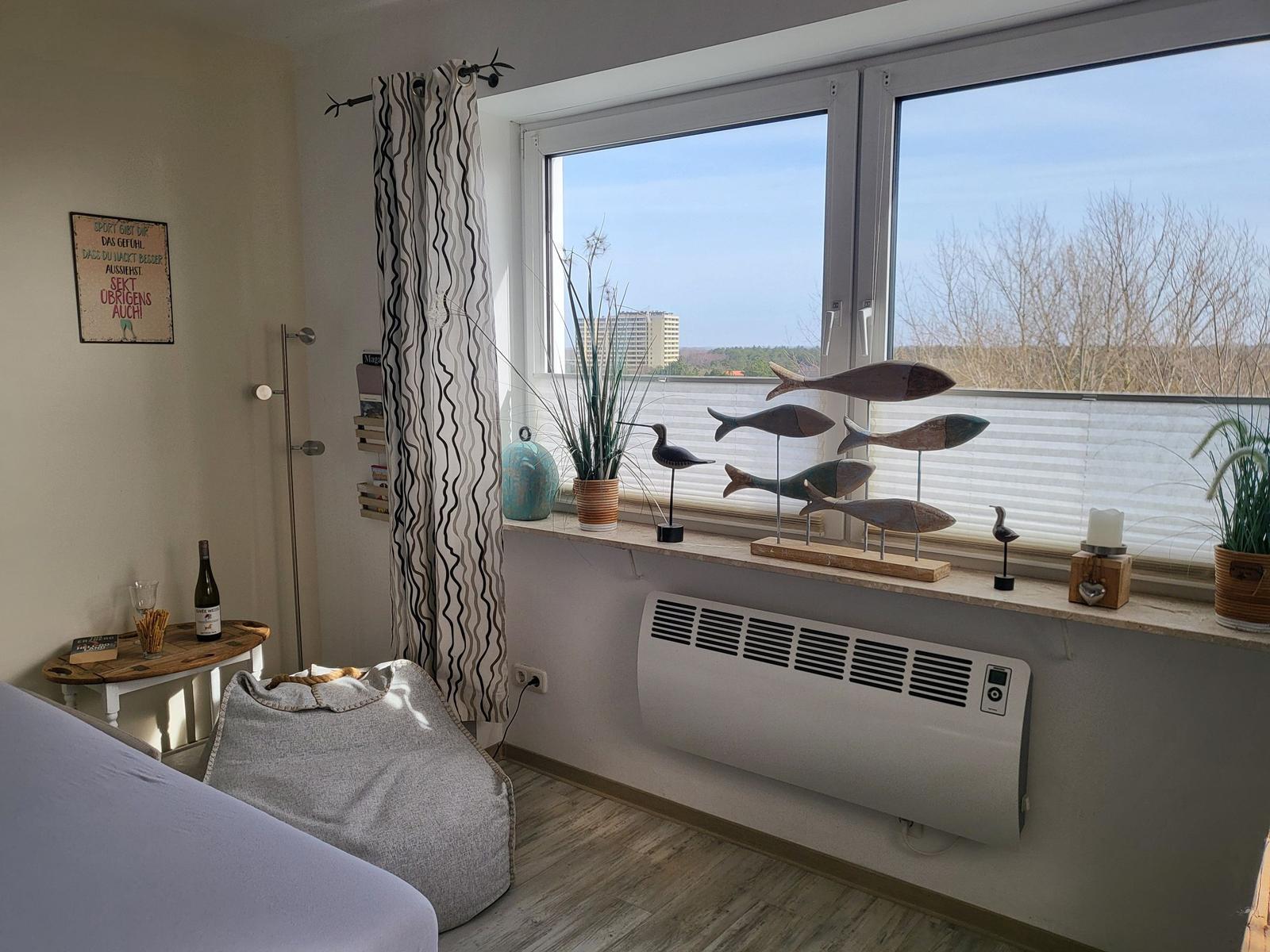 Zimmer mit Fenster, Sitzgelegenheit und Dekoration. Blick auf Gebäude und Bäume.