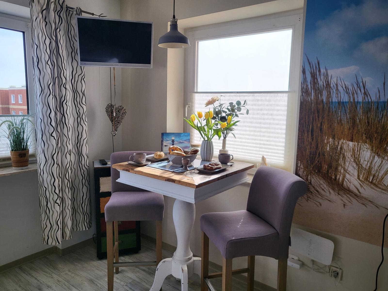 Esstisch mit zwei Stühlen, Fenster, Wandbild und Fernseher.