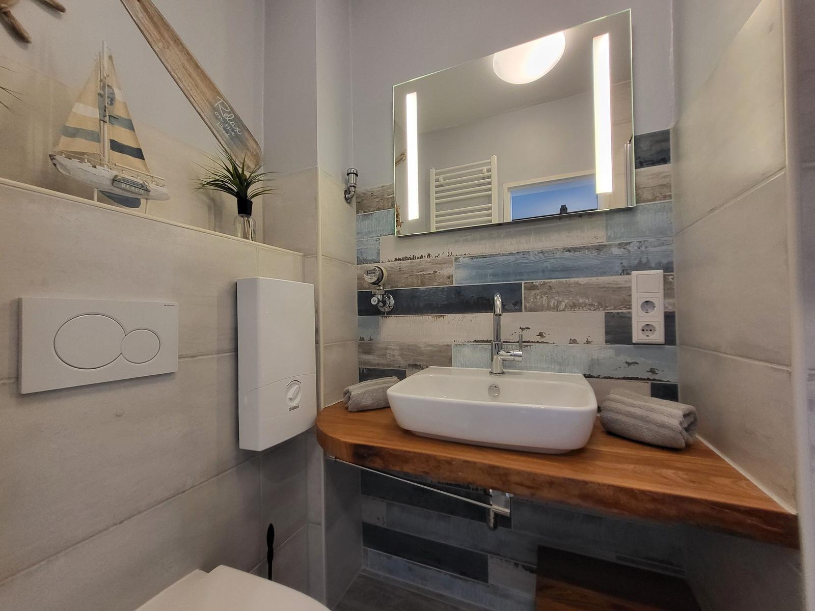 Badezimmer mit Waschbecken auf Holzplatte, Spiegel mit Beleuchtung und Segelboot-Dekoration.