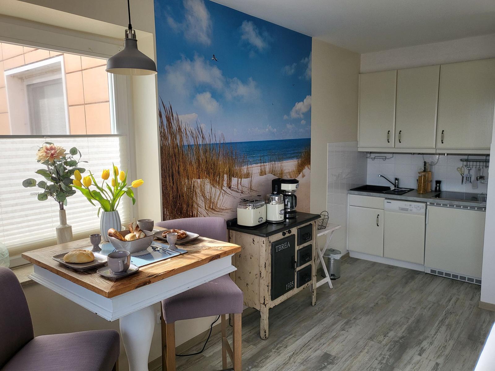 Küche mit Essbereich und Meeresmotiv-Wand. Holztisch, Stühle, Küchenschränke und Küchengeräte.