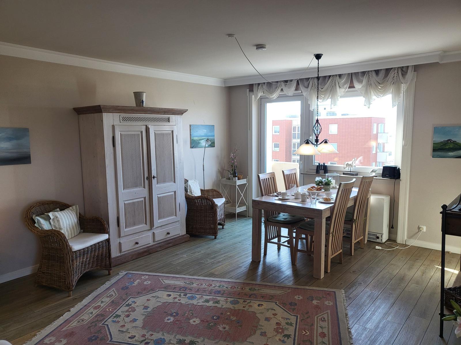Esszimmer mit Holztisch, Stühlen und Blick auf Gebäude. Wohnbereich mit Wickerstuhl und Kleiderschrank.