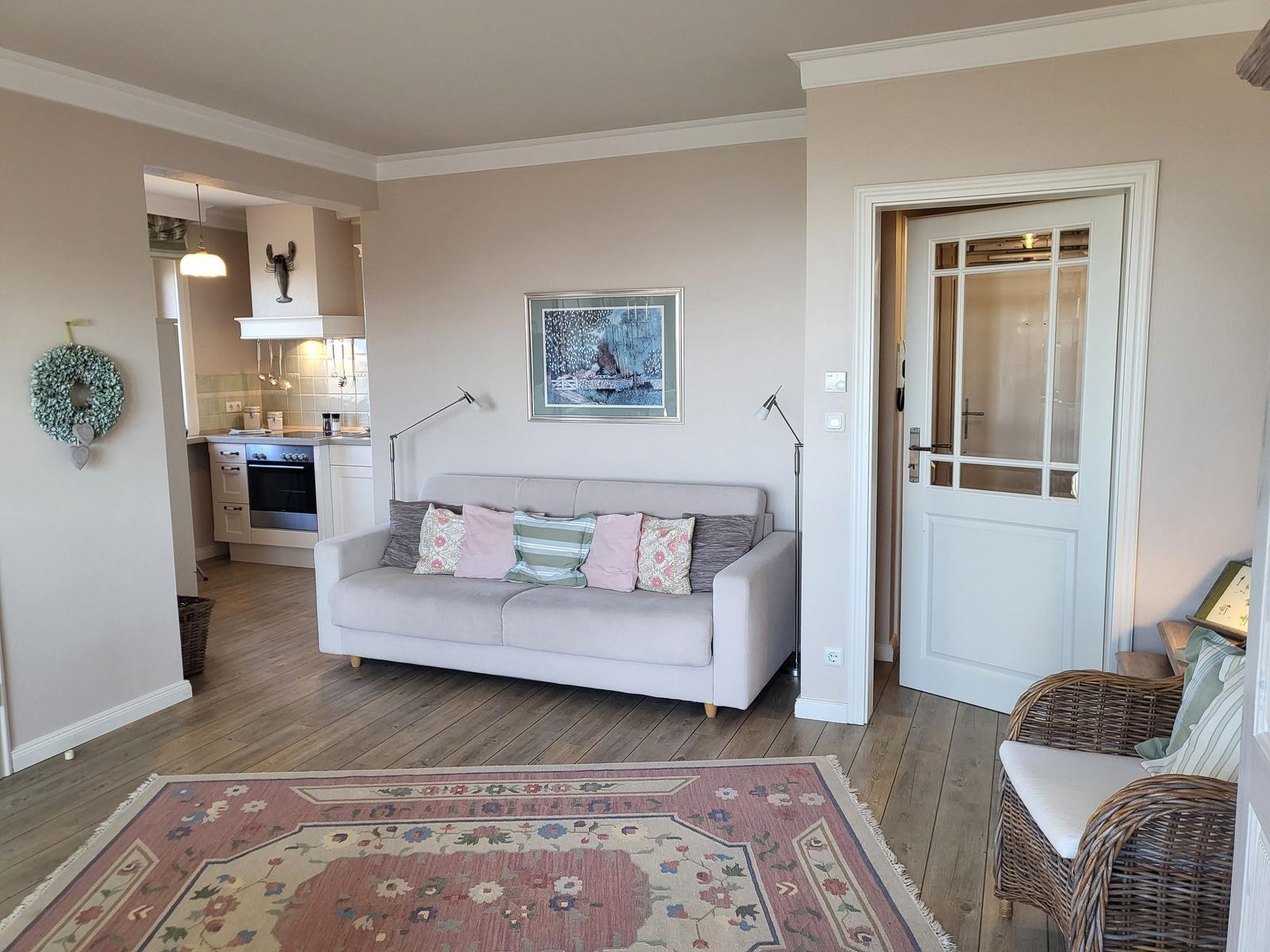Wohnzimmer mit Sofa, Teppich und Blick in die Küche.