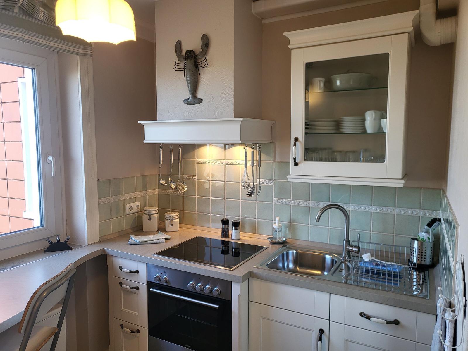 Küche mit Arbeitsplatte, Spüle, Herd und Glasfrontschrank.