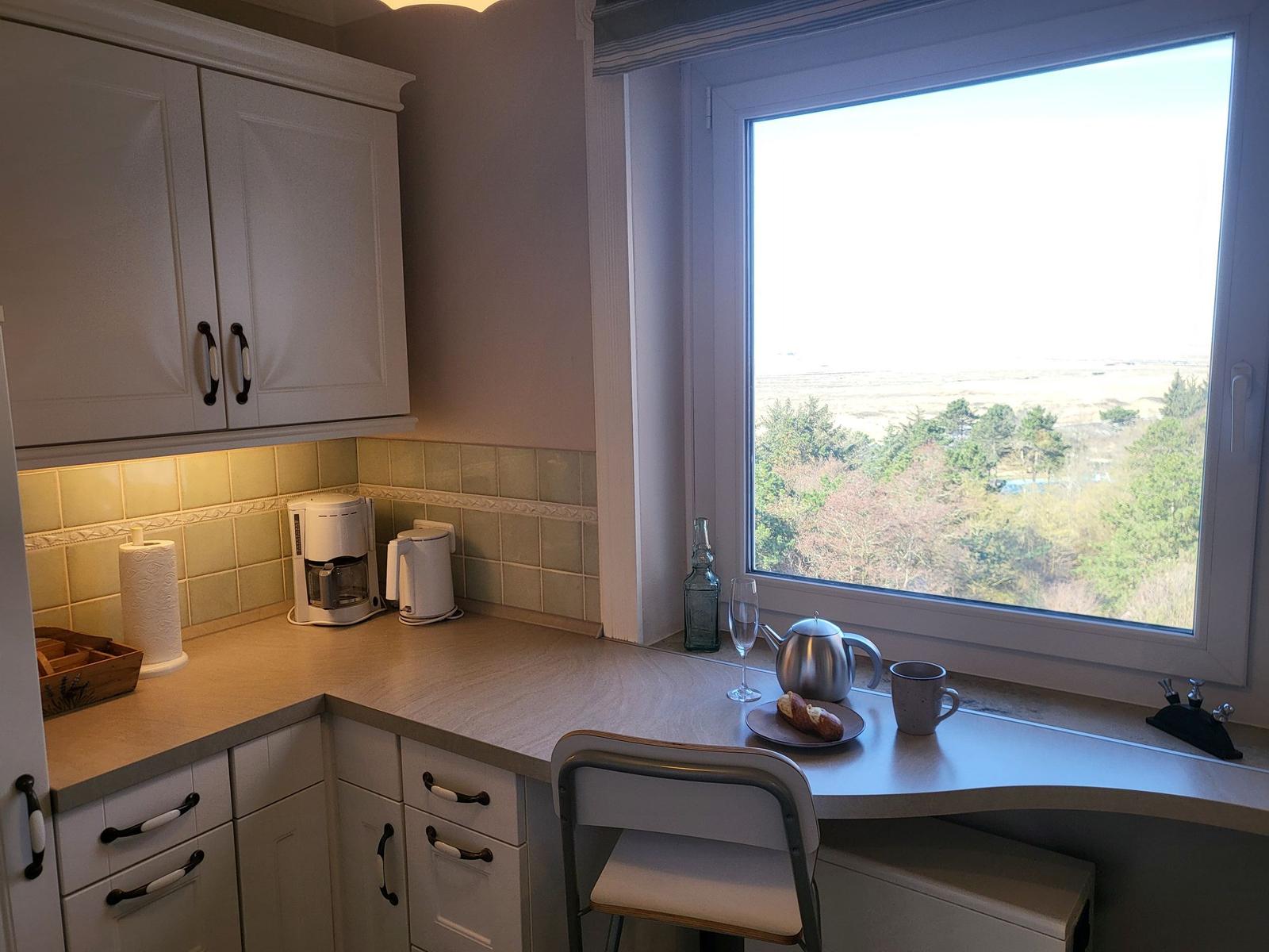 Küche mit Fensterblick auf Landschaft, Arbeitsplatz mit Kaffeemaschine und Teeutensilien.