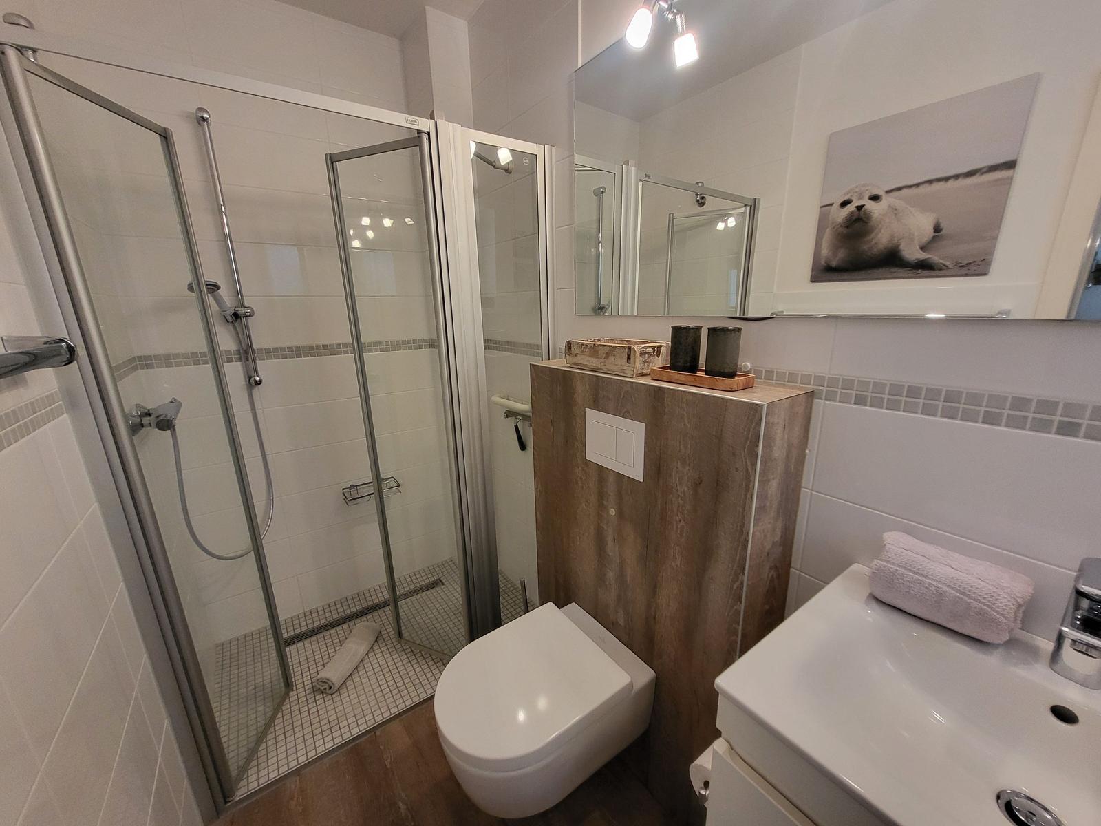 Badezimmer mit Dusche, Toilette und Waschbecken. Wandbild zeigt einen Seehund.