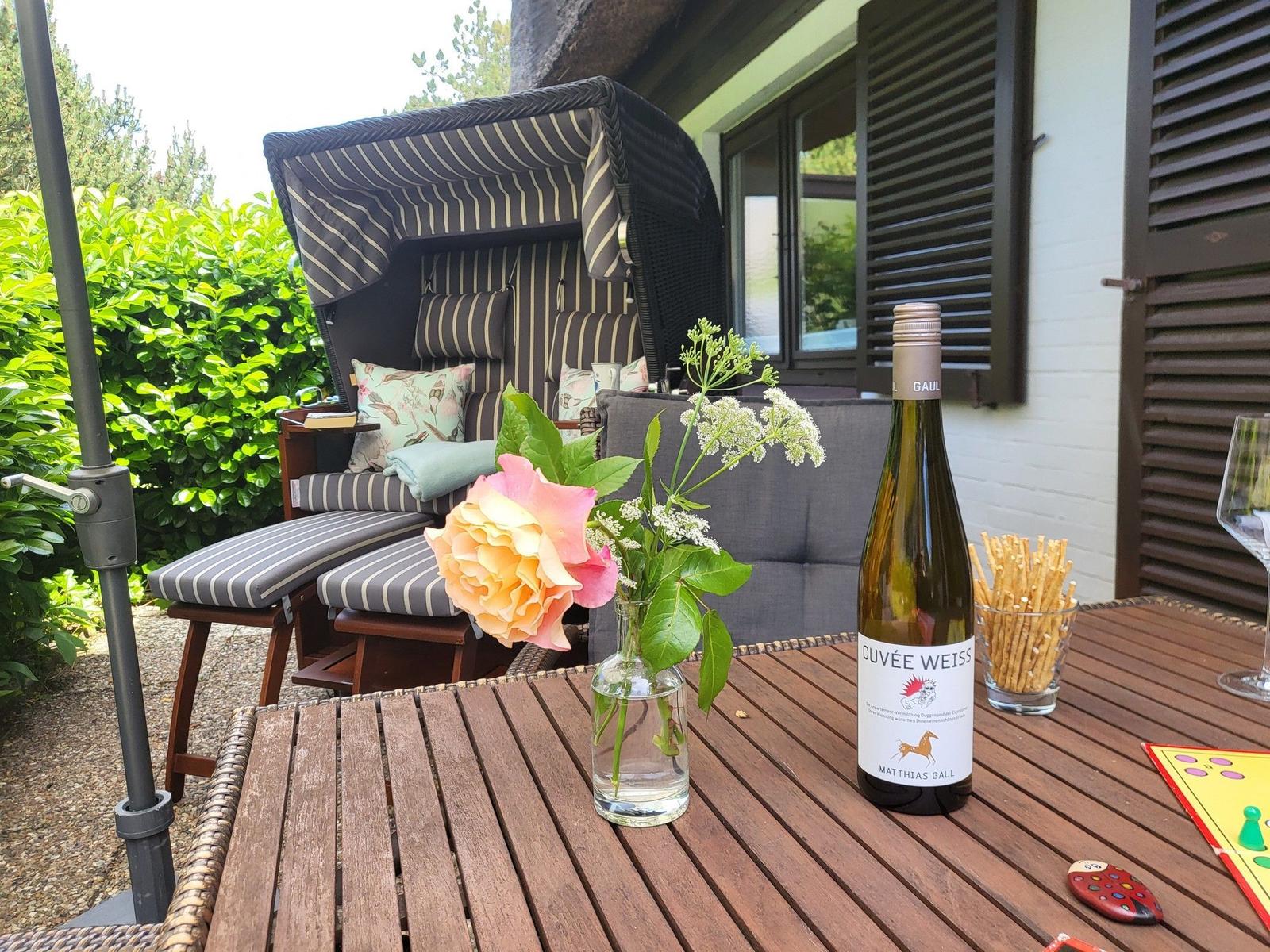 Terrasse mit Liege, Tisch und Wein. Blumen und Snacks auf dem Tisch.