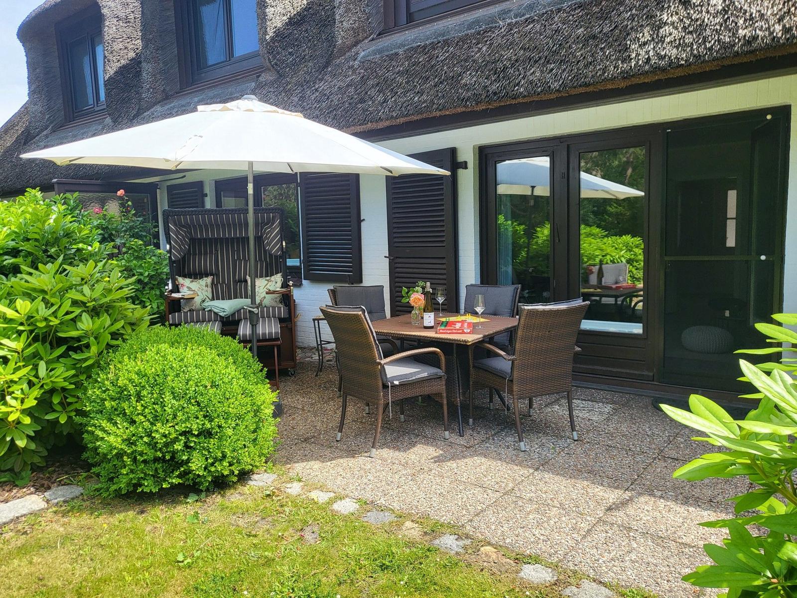 Terrasse mit Tisch, Stühlen und Sonnenschirm neben einem Haus mit Strohdach.
