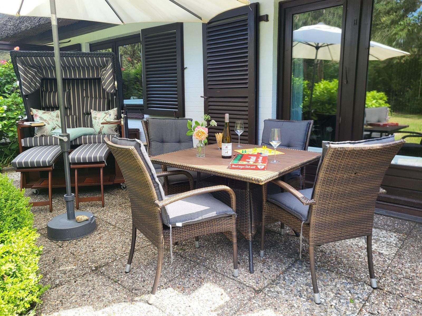 Terrasse mit Sitzgruppe, Tisch und Sonnenschirm. Hintergrund: Haus mit Fenstern und Pflanzen.