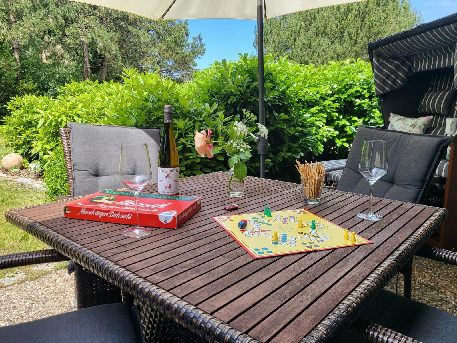 Außentisch mit Brettspiel, Wein und Stühlen unter Sonnenschutz.