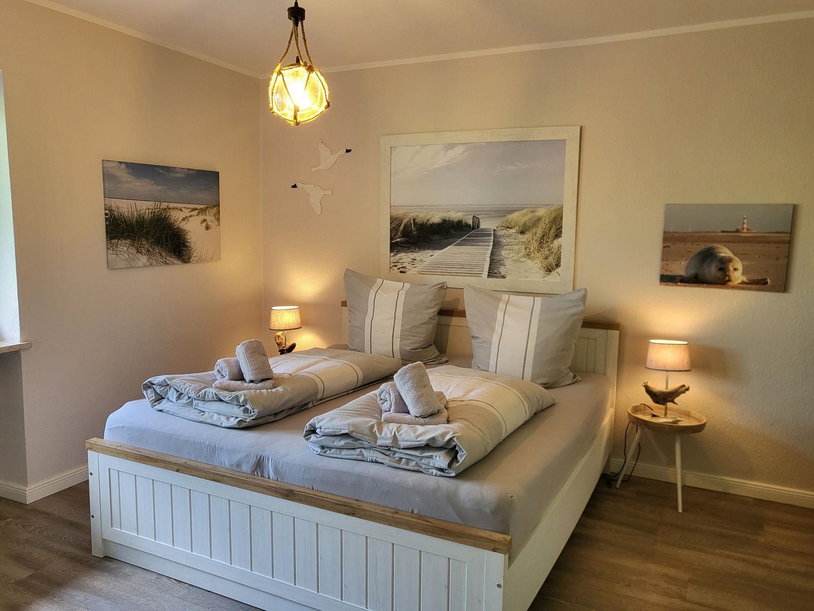 Schlafzimmer mit Doppelbett, Strandmotiven an den Wänden und zwei Nachttischen mit Lampen.