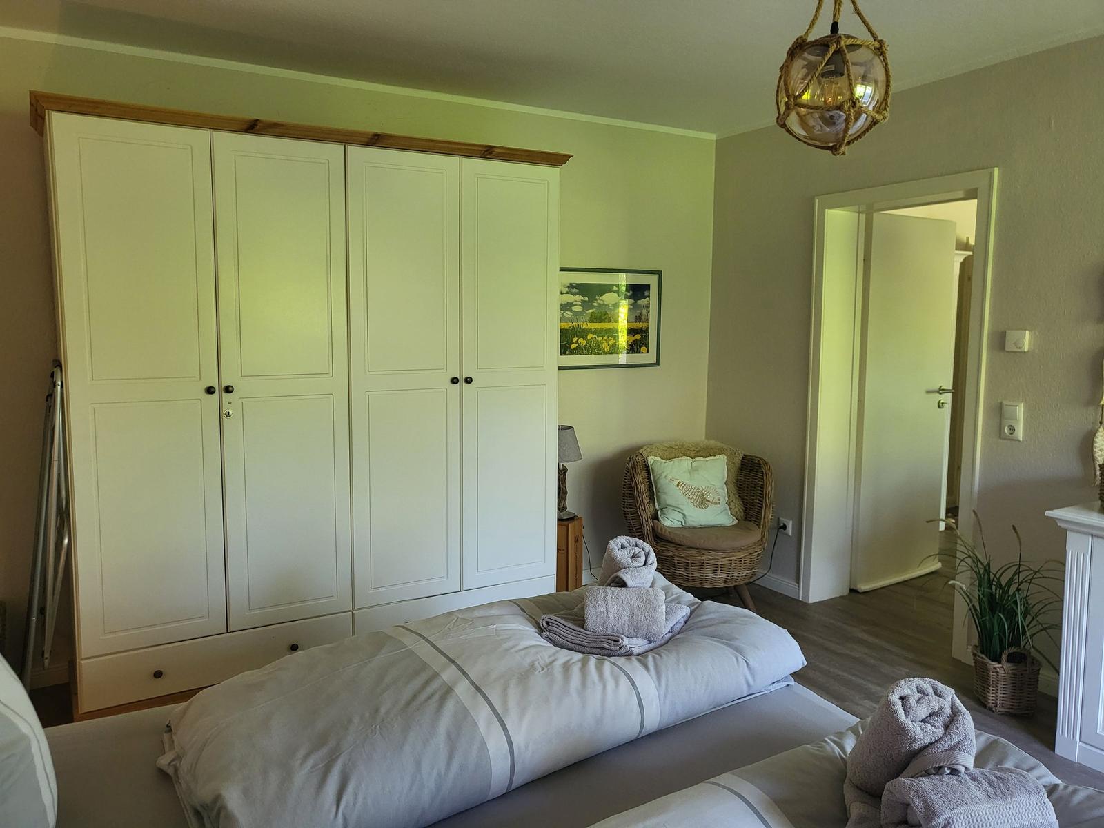 Schlafzimmer mit Doppelbett, Kleiderschrank und Sessel. Decke mit Hängelampe.