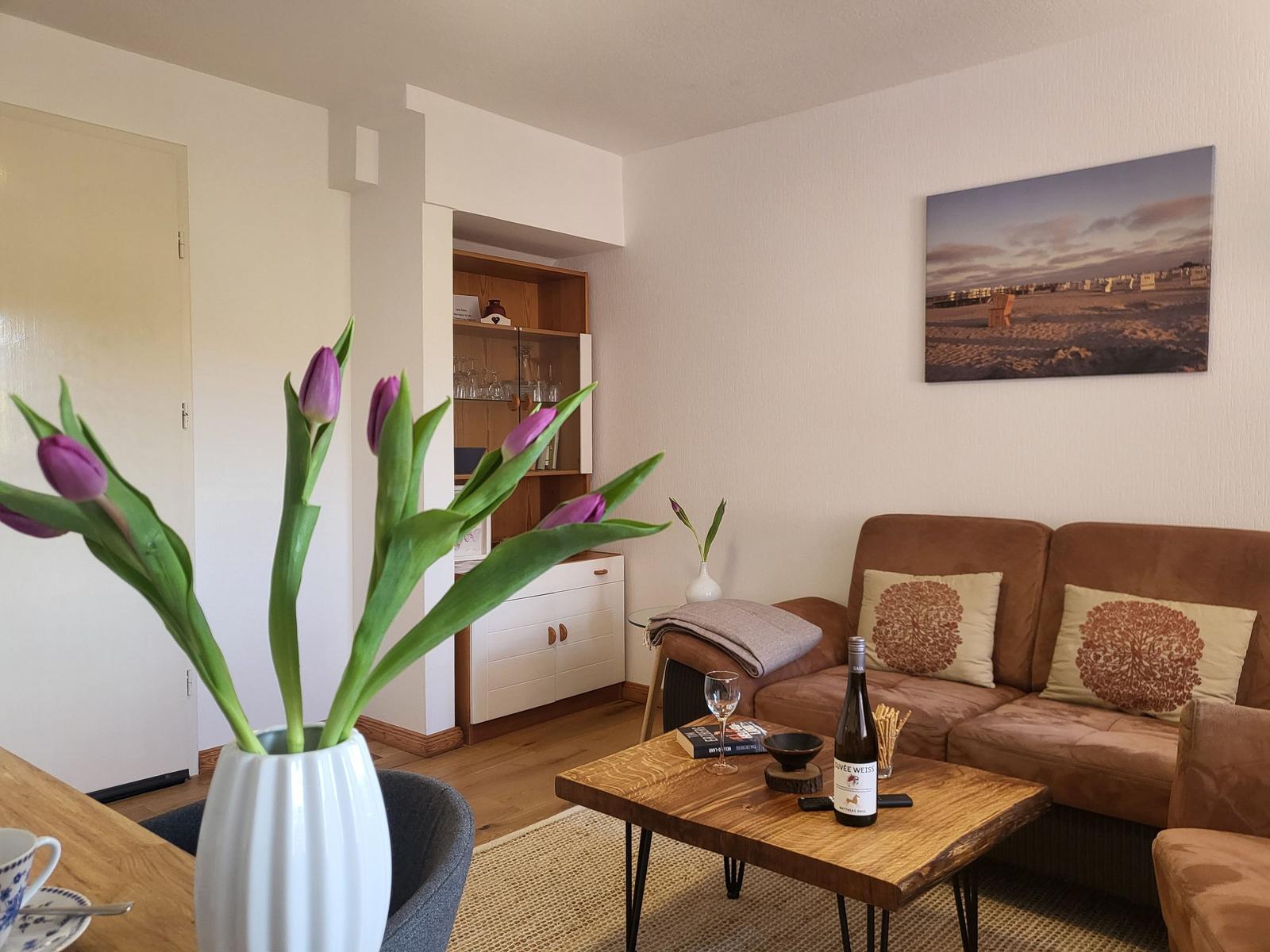 Wohnzimmer mit Sofa, Couchtisch und Tulpen im Vordergrund.
