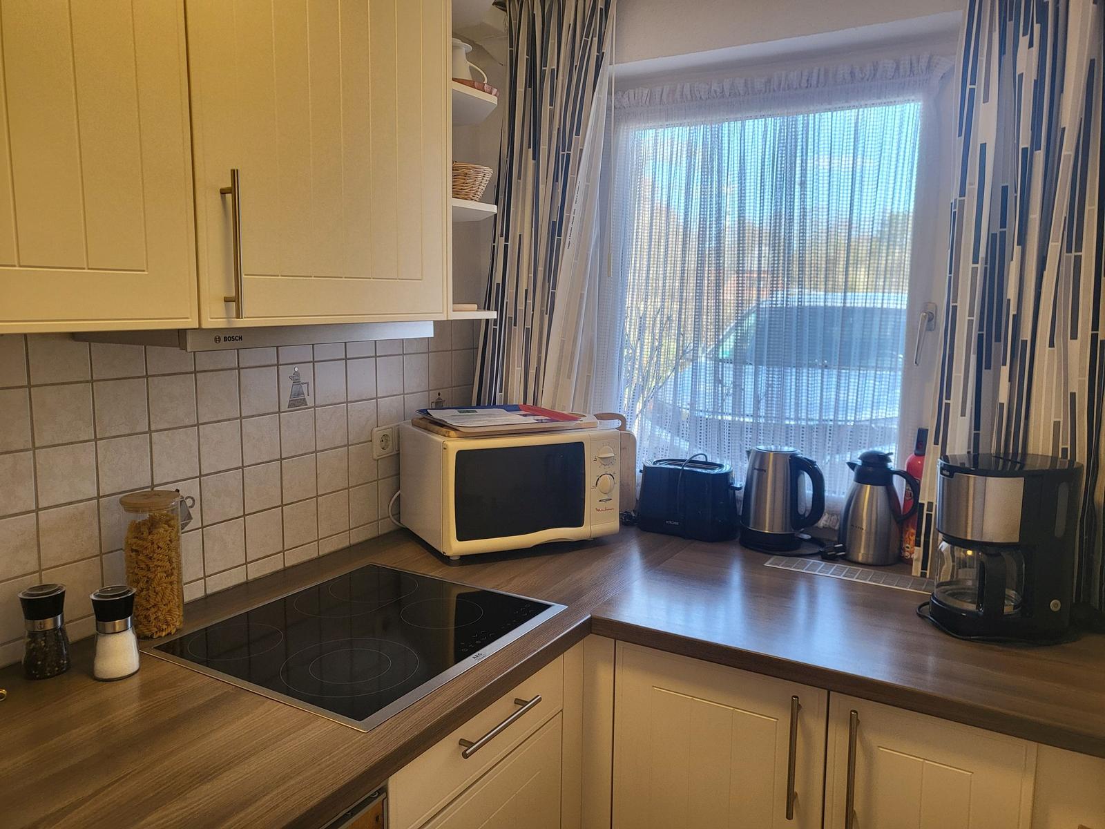 Küche mit Herd, Mikrowelle, Kaffeemaschine und Fenster mit Vorhängen.