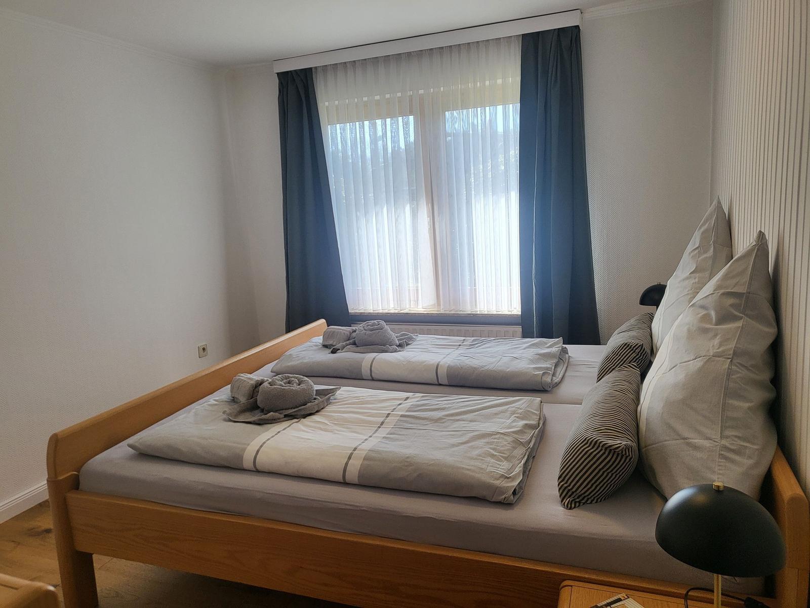 Ein Schlafzimmer mit einem Doppelbett, Fenster mit Vorhängen und einer Nachttischlampe.