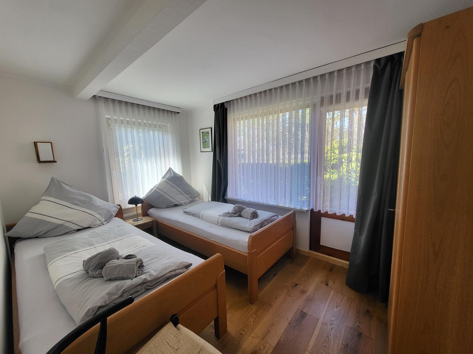 Zwei Einzelbetten mit Bettwäsche, Holzfußboden und Fenster mit Vorhängen.