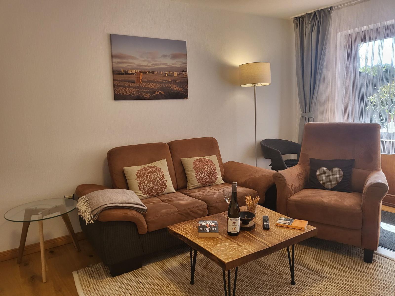 Wohnzimmer mit braunem Sofa, Sessel und Holztisch. Wandbild und Fenster mit Vorhängen.