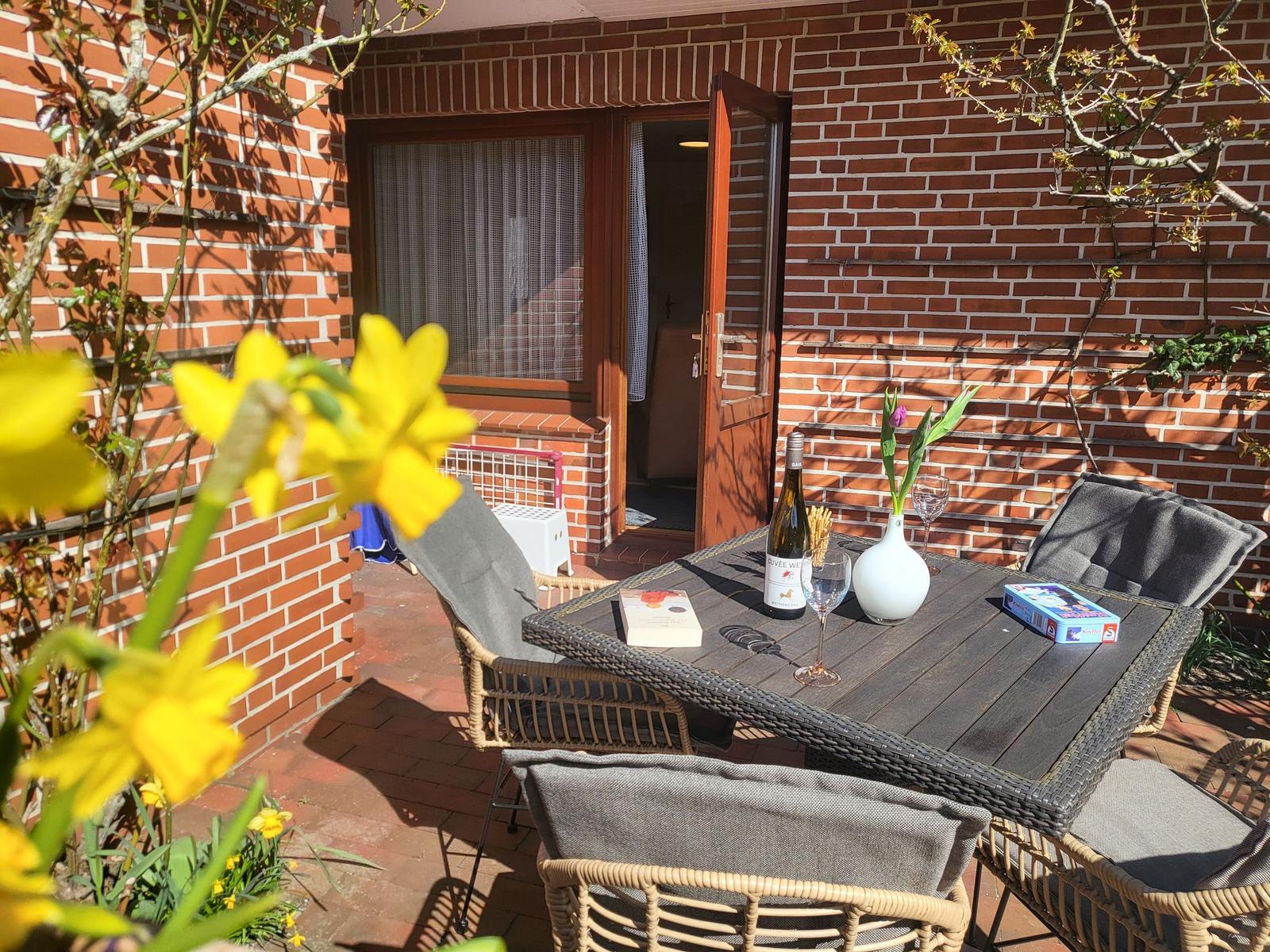 Terrasse mit Tisch, Stühlen und Blumen. Tür führt ins Haus.