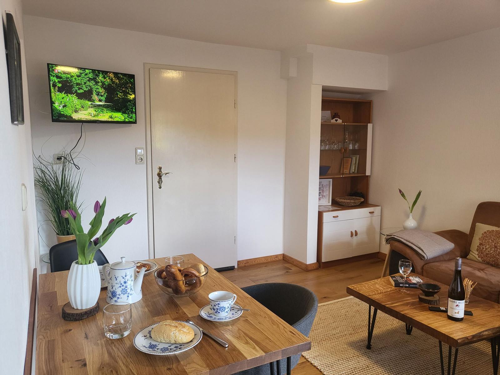 Esszimmer mit Tisch, Stühlen und Fernseher. Wohnbereich mit Couch, Tisch und Schrank.