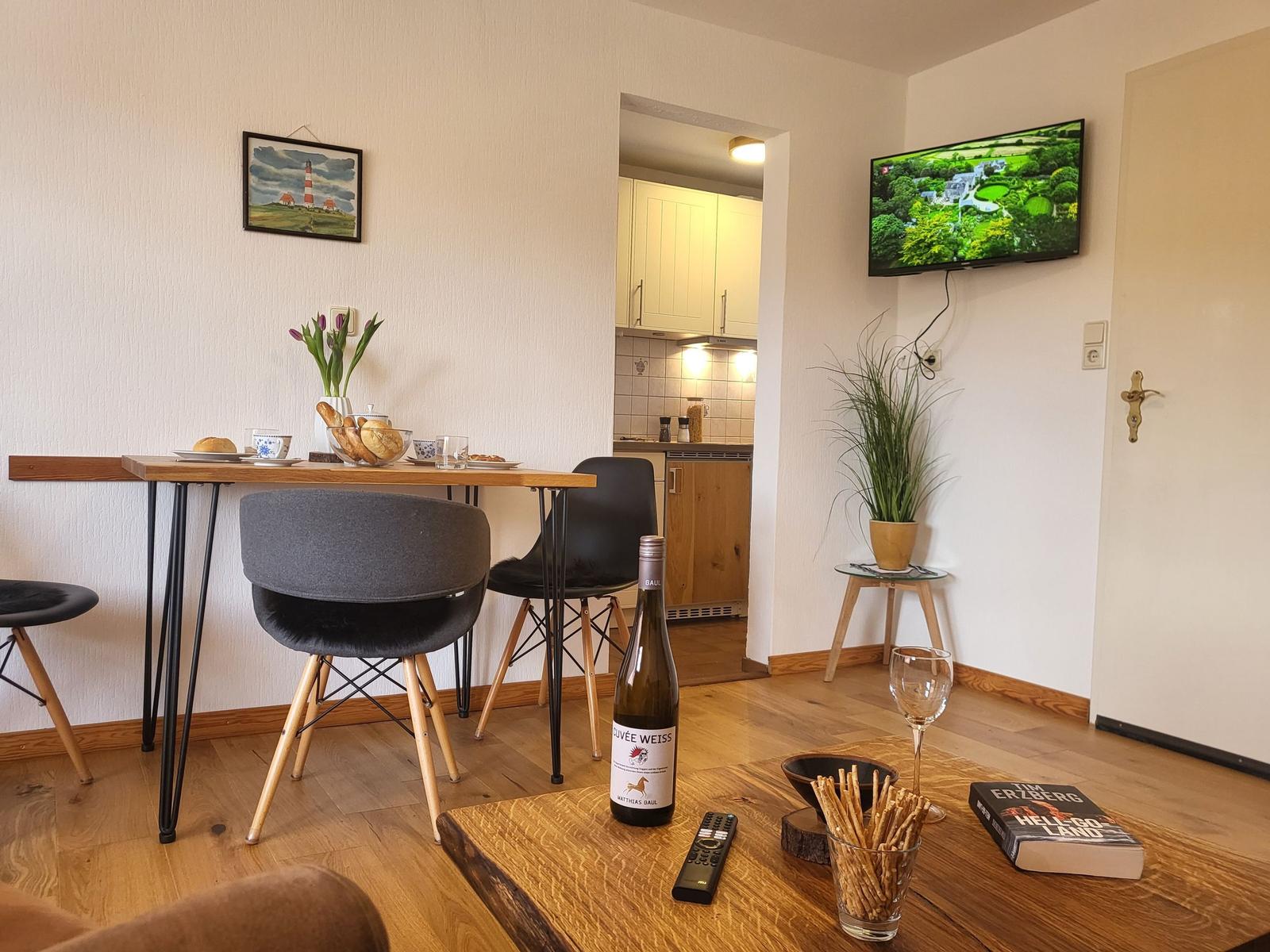 Wohnbereich mit Esstisch, Fernseher und Küchenbereich im Hintergrund.