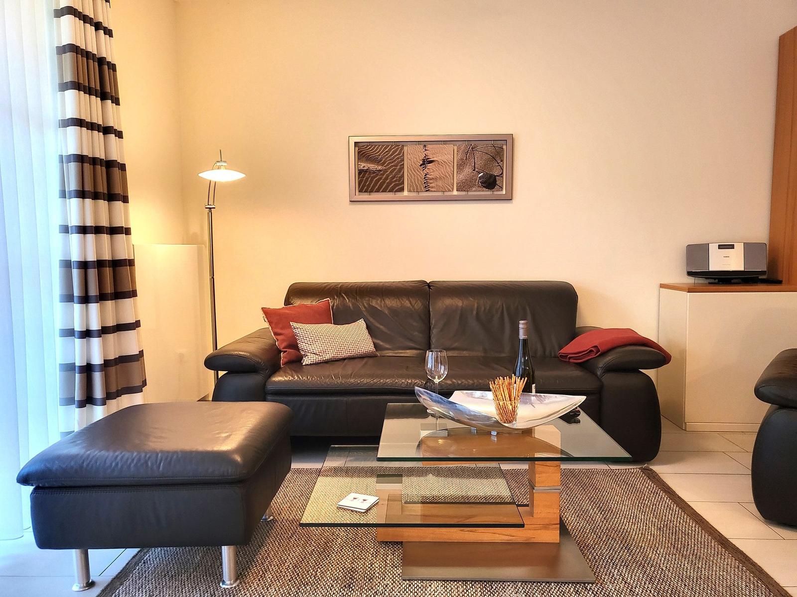 A living room with a black leather sofa, a glass table, and an ottoman.