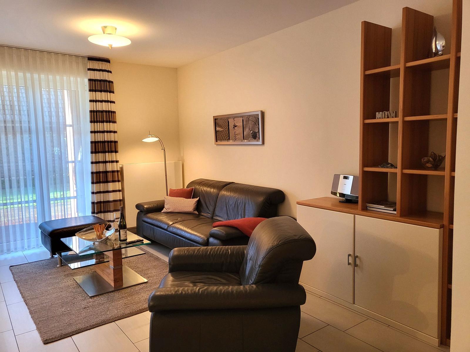 Living room with leather sofa, glass table, and wooden wall shelf.