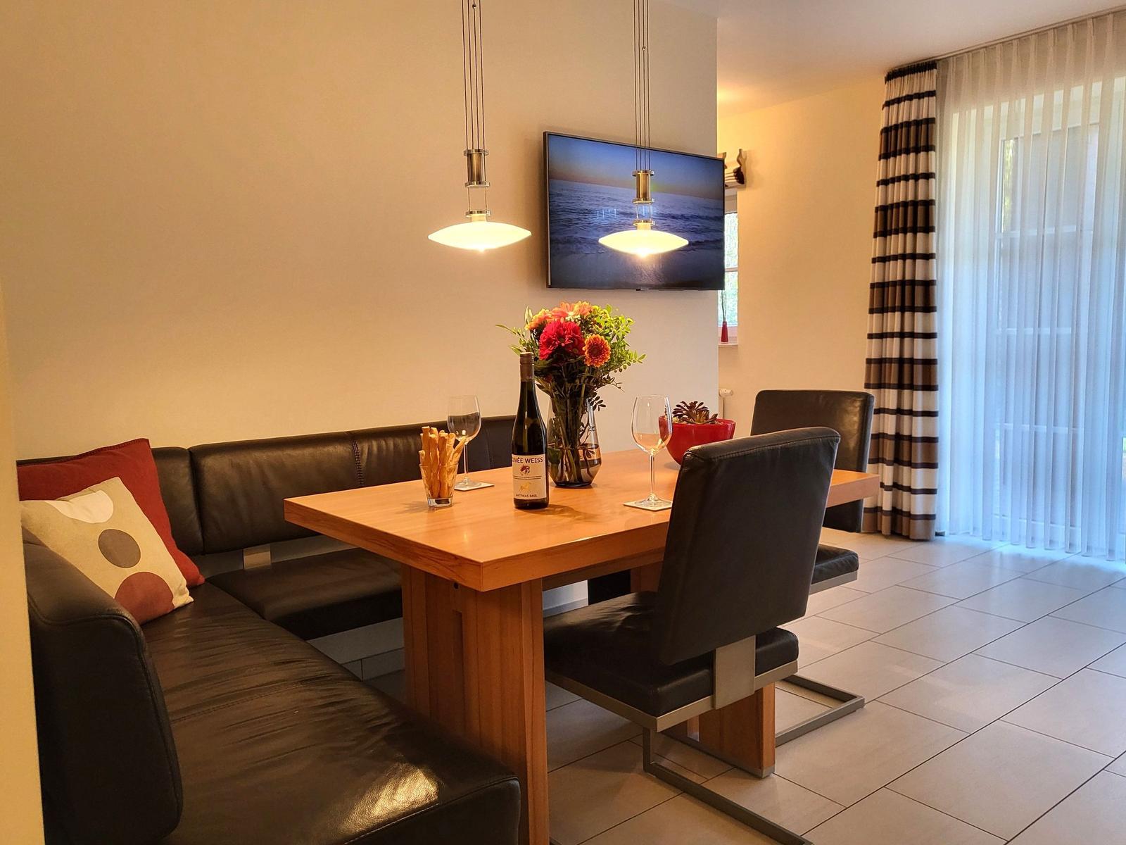 Dining room with wooden table, black chairs, and sofa. Wall-mounted TV and window with curtains.