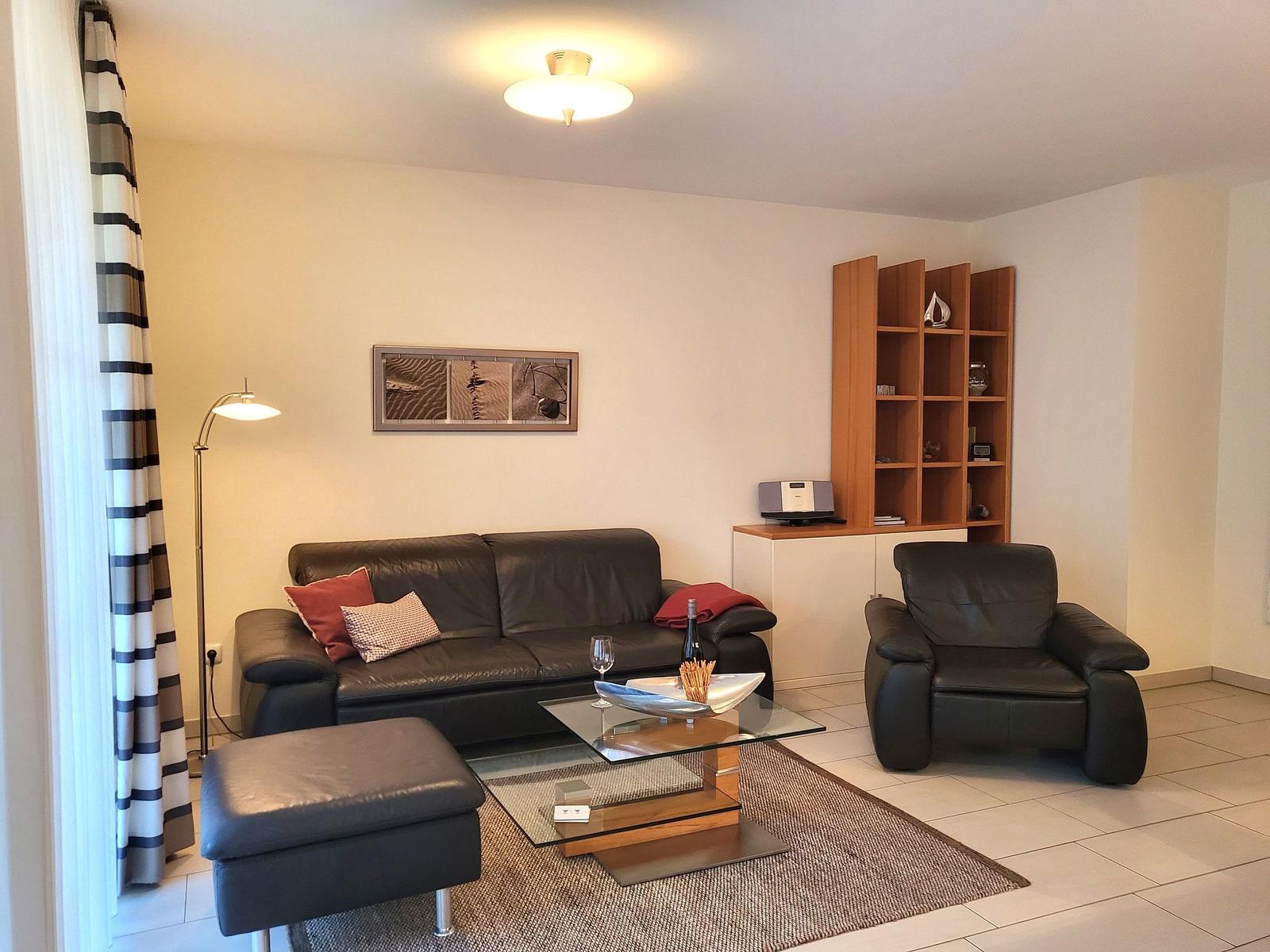 A living room with leather sofa, armchair, and glass table. A picture hangs on the wall.