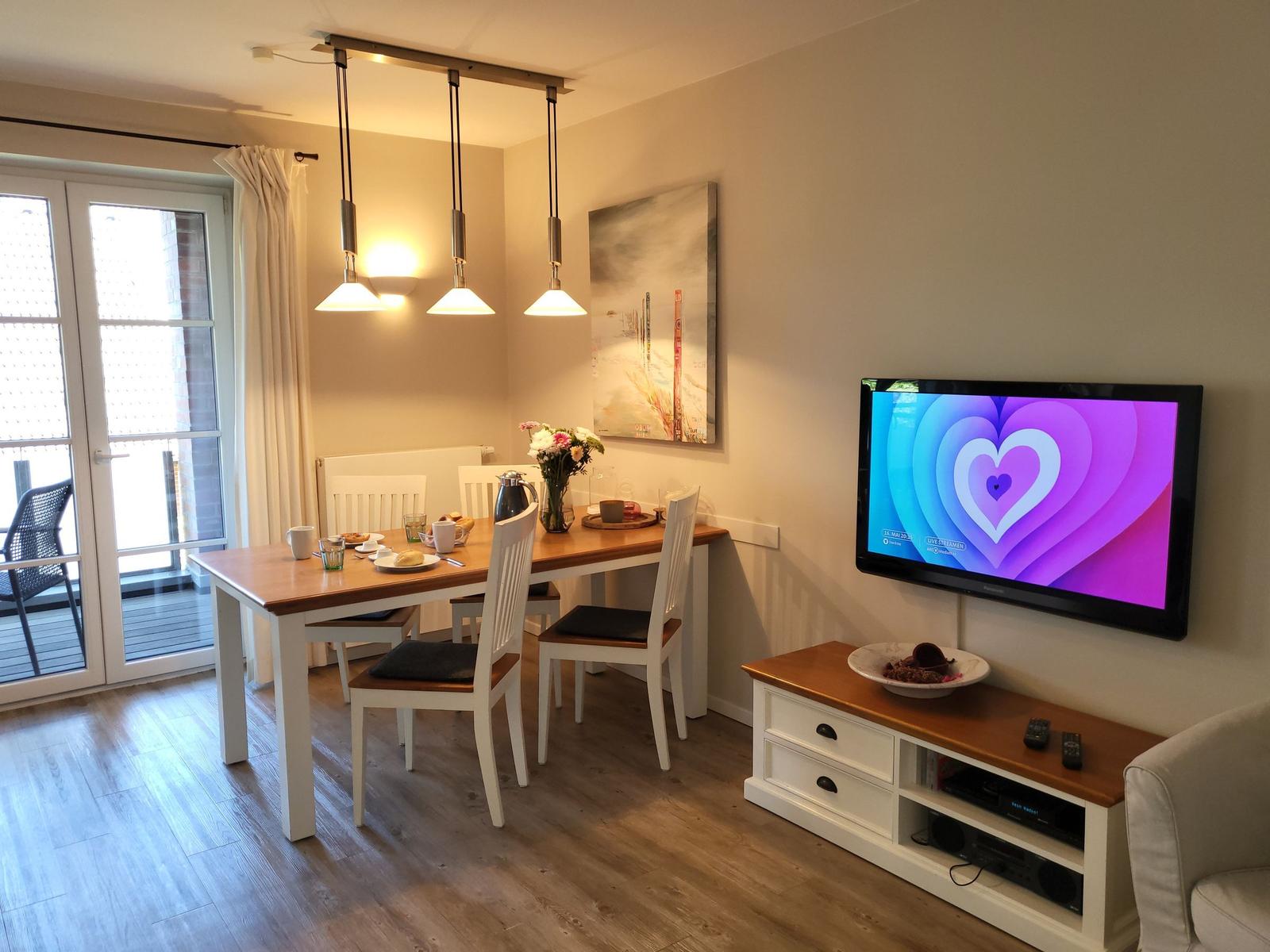 Esszimmer mit Tisch, Stühlen und Fernseher an der Wand.