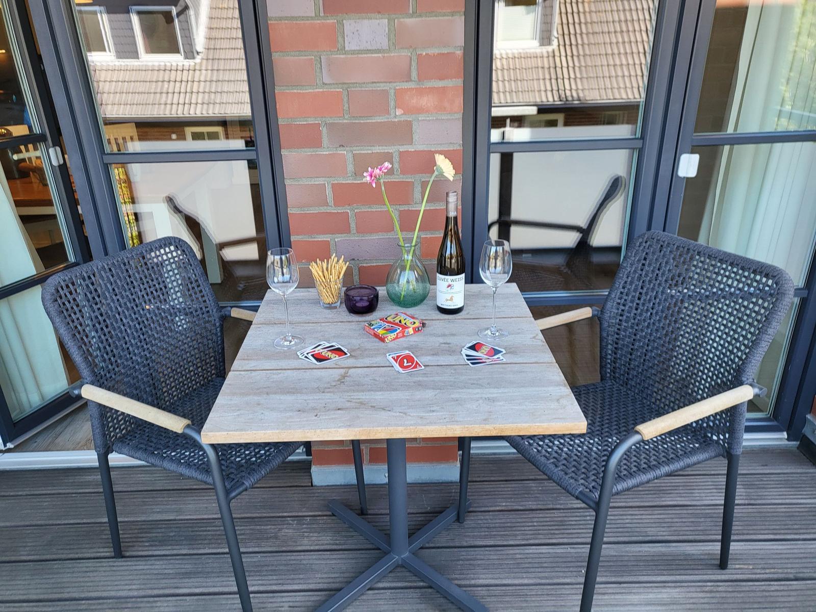 Tisch mit zwei Stühlen, Wein, Karten und Blumen auf Balkon