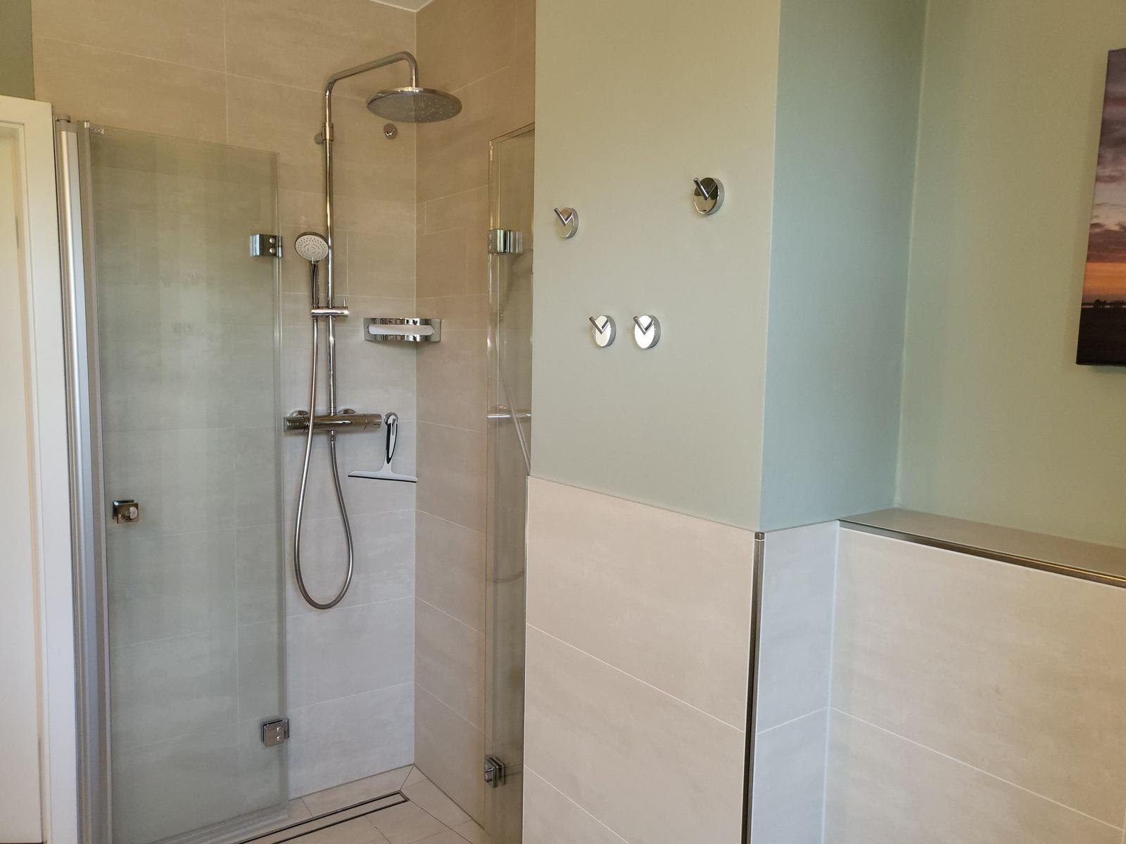 Dusche mit Glaswand, Duschbrause und Steuerungselementen an der Wand.