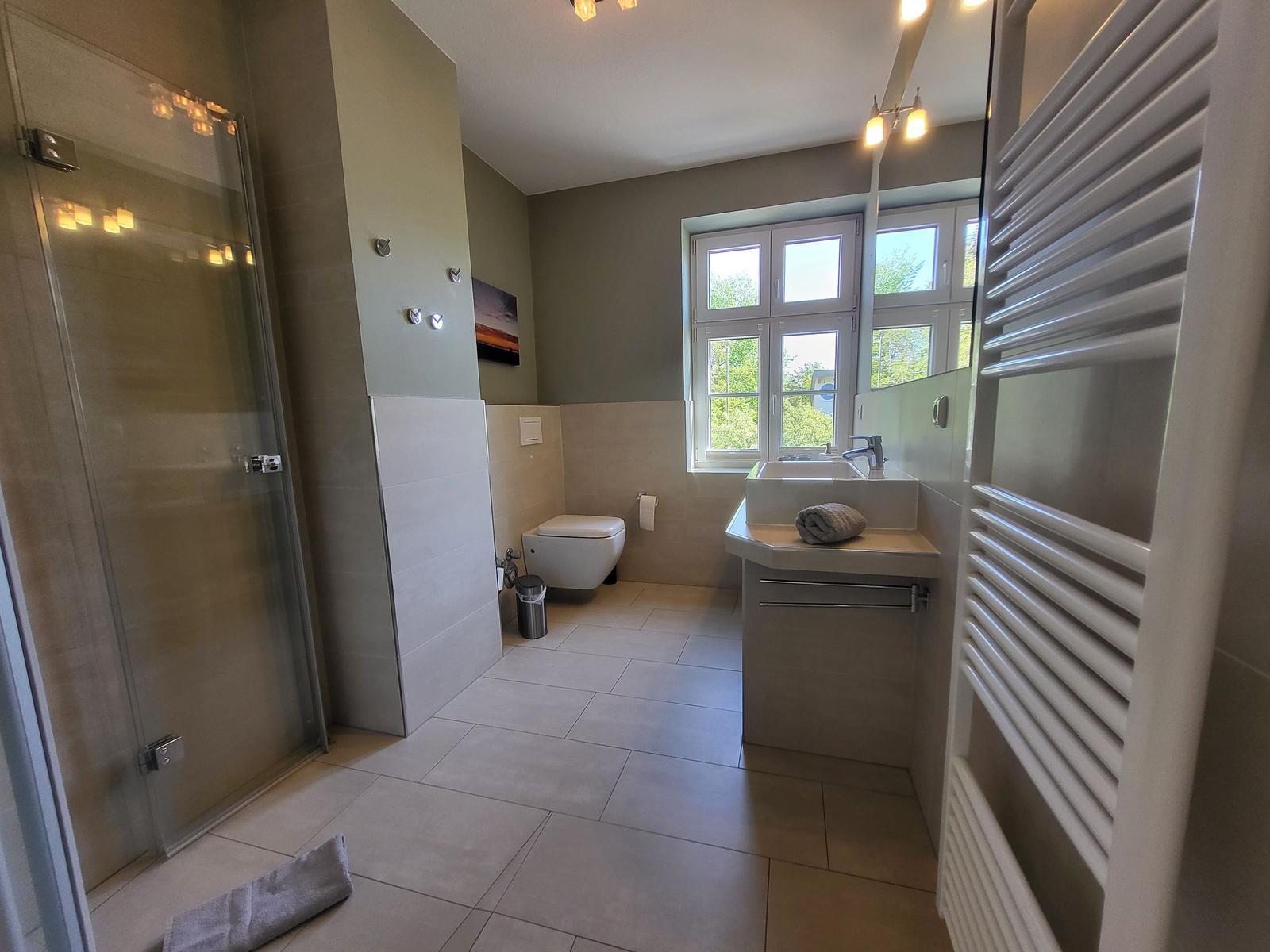 Badezimmer mit Dusche, Toilette und Waschbecken. Fenster mit Blick auf Grün.